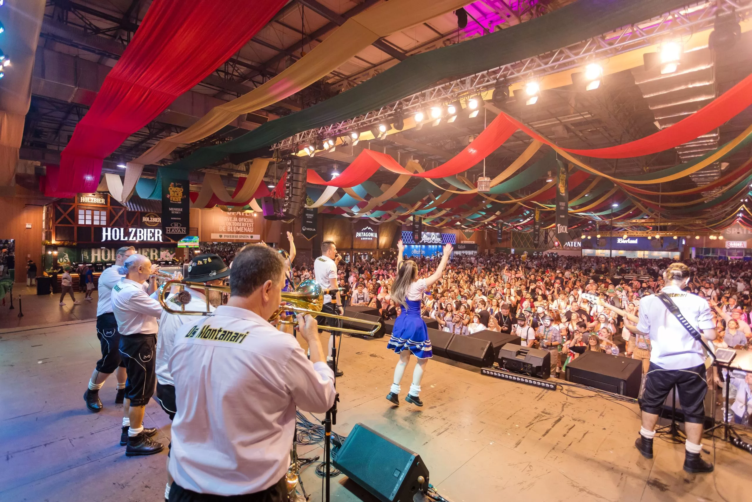 Foto na Oktoberfest Blumenau, um palco onde há pessoas festejando. Na frente aparece o público, uma multidão